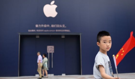 A boy holds a Chinese flag as he walks past an Apple Store undergoing renovation in Beijing on July 18, 2018.