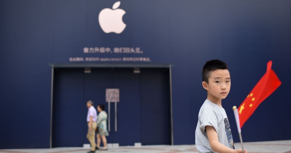 A boy holds a Chinese flag as he walks past an Apple Store undergoing renovation in Beijing on July 18, 2018.