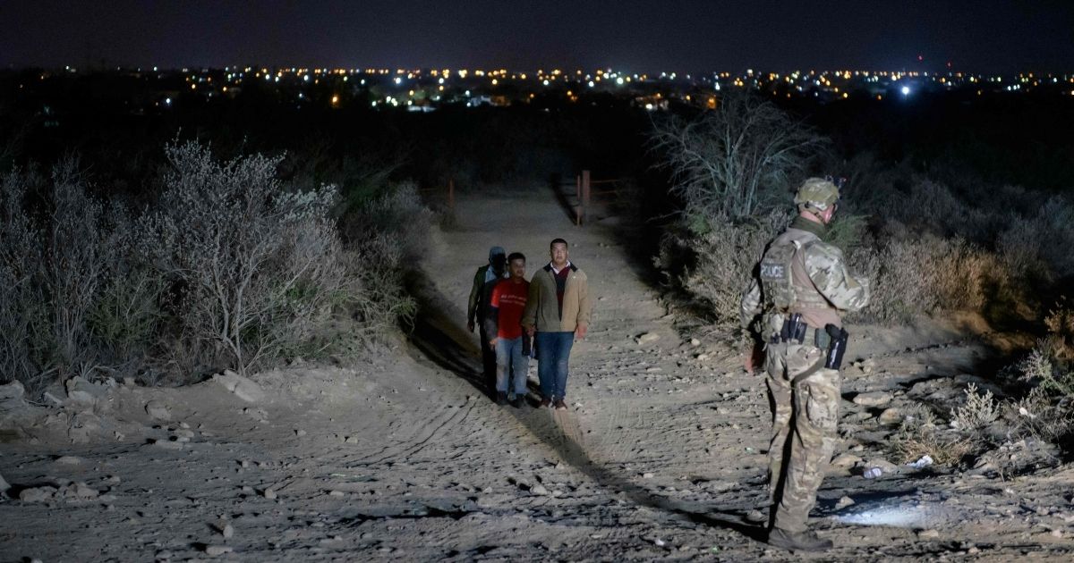 Illegal immigrants who arrived across the Rio Grande river from Mexico make their way along a track past a US border patrol agent on March 27, 2021 towards a makeshift processing checkpoint before being detained at a holding facility in the border city of Roma, Texas.