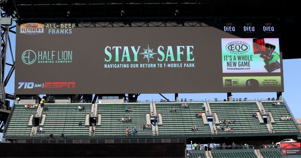 COVID-19 messages are shown on a screen behind socially distanced fans before a game between the Seattle Mariners and Houston Astros at T-Mobile Park on April 17.