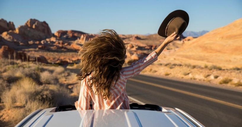 This stock photo portrays a woman driving through the desert, standing up and looking through the car's sunroof. Just in time for Memorial Day travel this year, America is paying the highest price for a gallon of gas since 2014.