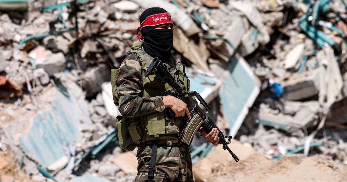 A masked fighter with the National Resistance Brigades, the military wing of the Democracy Front Liberation of Palestine, stands in front of the ruins of the al-Jalaa tower in Gaza City on Sunday.