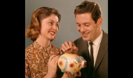 A smiling 1960s couple puts coins into a piggy bank.