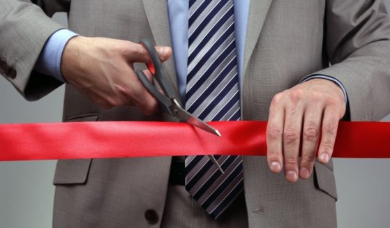A man is pictured cutting through red tape in the stock image above.