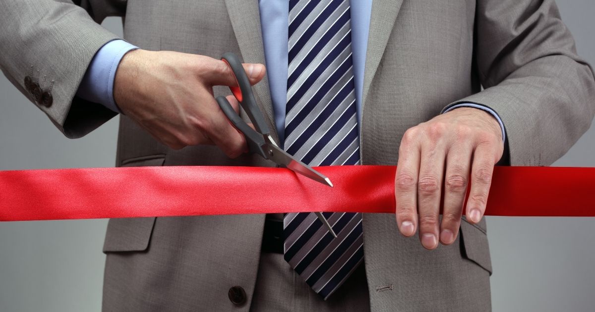 A man is pictured cutting through red tape in the stock image above.