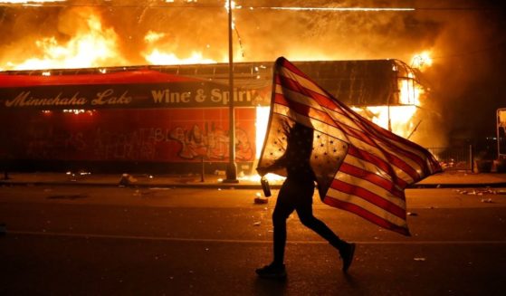 A protester carries a U.S. flag upside down next to a burning building in Minneapolis on May 28, 2020, during riots over the death of George Floyd.