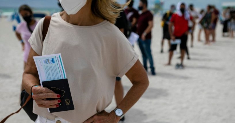 A woman holds her passport as she waits in line to get the Johnson & Johnson COVID-19 vaccine at a pop-up vaccination center at the beach, in South Beach, Florida, on May 9, 2021.