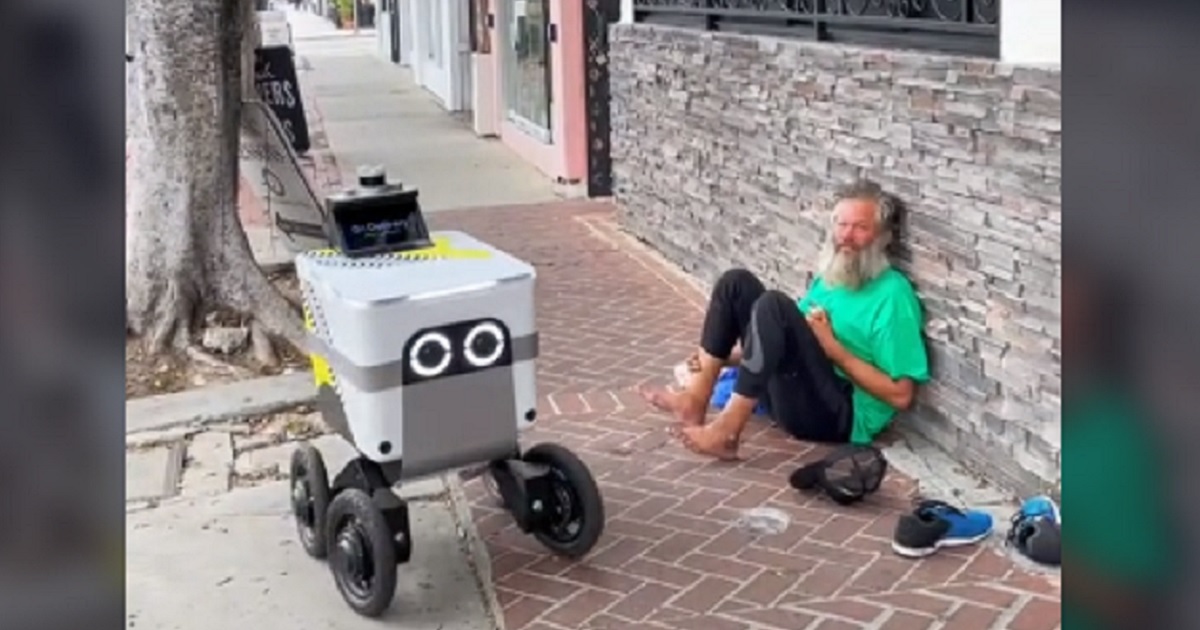 A food delivery robot rolls past a barefoot bearded man sitting on a sidewalk in Los Angeles in a video posted to TIkTok last week.