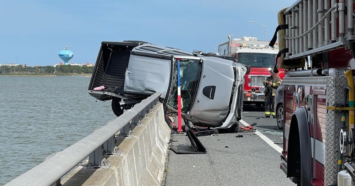 A truck teeters on the edge of a guardrail after a car accident