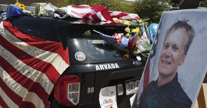 Flowers, flags and notes cover a patrol car and bike outside Arvada City Hall during a memorial for Arvada police officer Gordon Beesley on Tuesday in Arvada, Colorado.