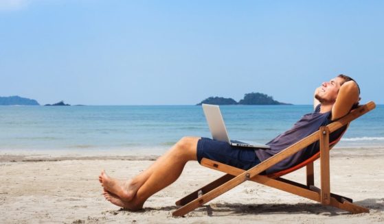 Happy businessman is pictured with his laptop relaxing on the beach.
