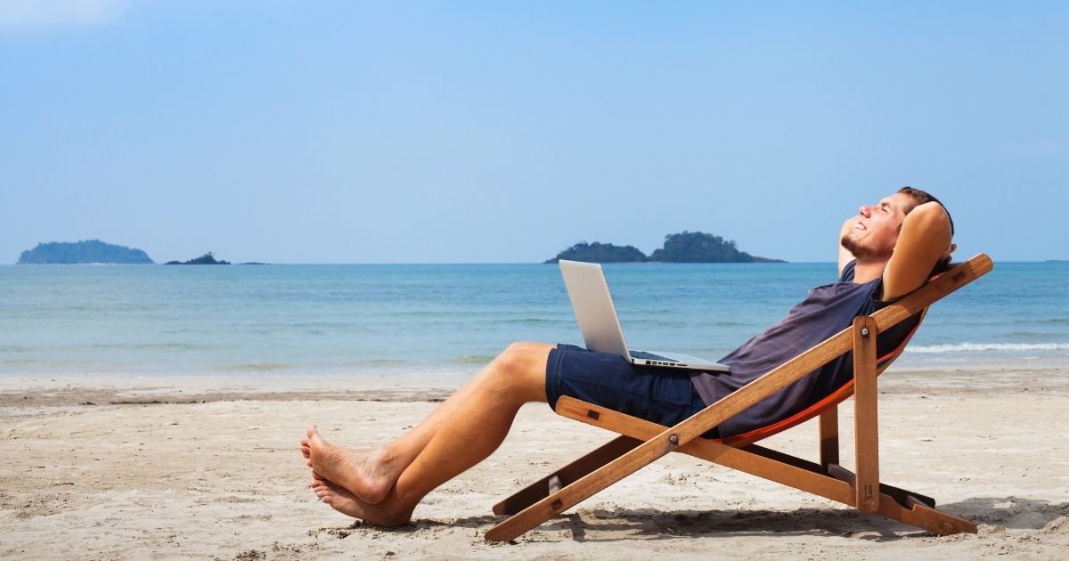 Happy businessman is pictured with his laptop relaxing on the beach.