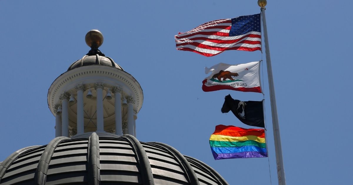 The rainbow Pride flag flutters below the U.S. and California flags at the state Capitol in Sacramento on June 17, 2019.