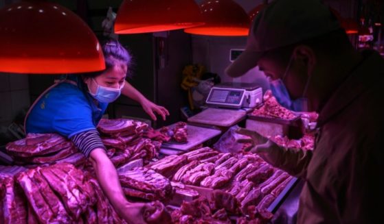 A Chinese meat vendor wears a protective mask as she serves a customer at her stall at a food market on April 24, 2020, in Beijing.