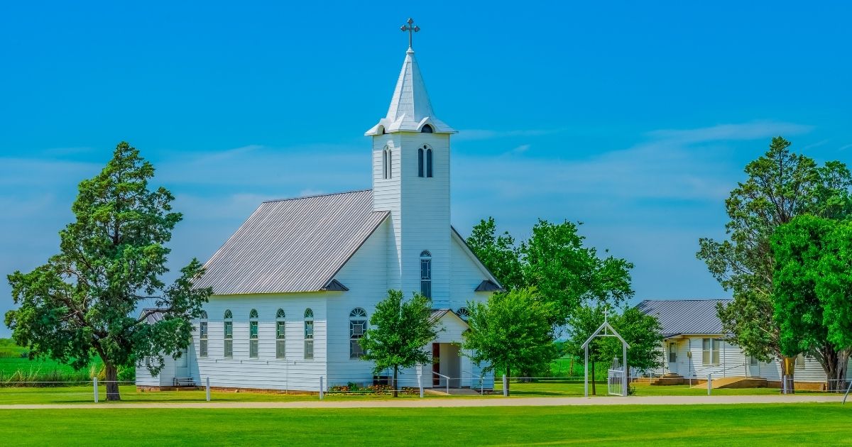 A steepled white church sits in a spring meadow in Texas. Trees surround the Christian chapel.