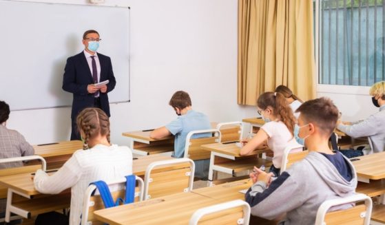 A teacher is pictured in a classroom with his students in the stock image above.