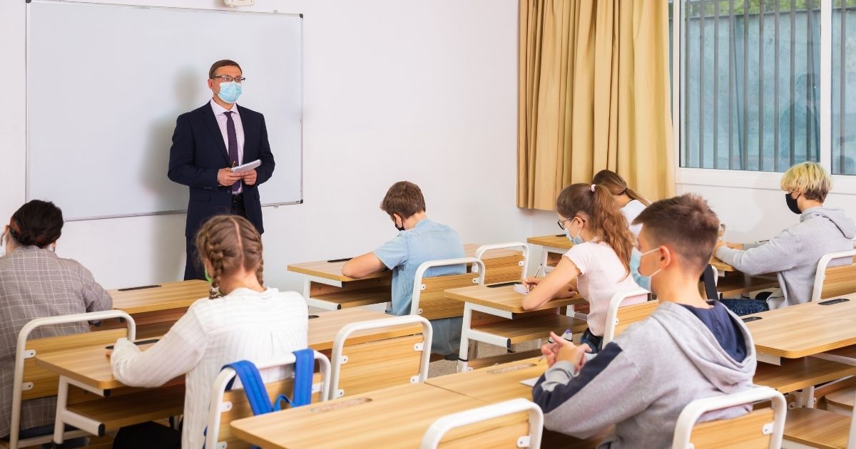 A teacher is pictured in a classroom with his students in the stock image above.