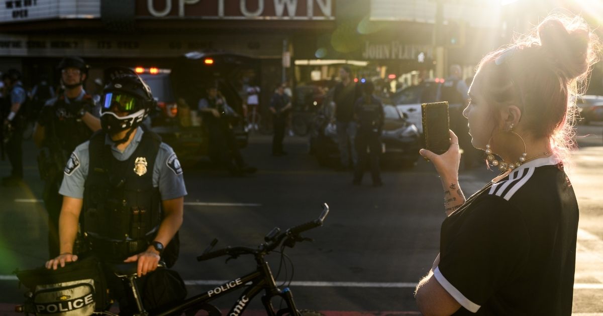 A woman appears to record police officers with her phone as they clear an intersection where protesters were staging an anti-police demonstration on June 4 in Minneapolis.