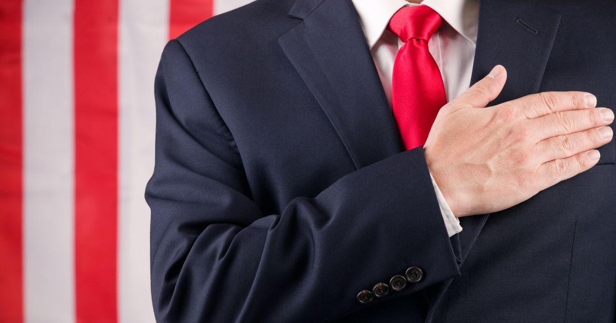 The above stock photo shows a man in front of the American flag, saying the pledge of allegiance.