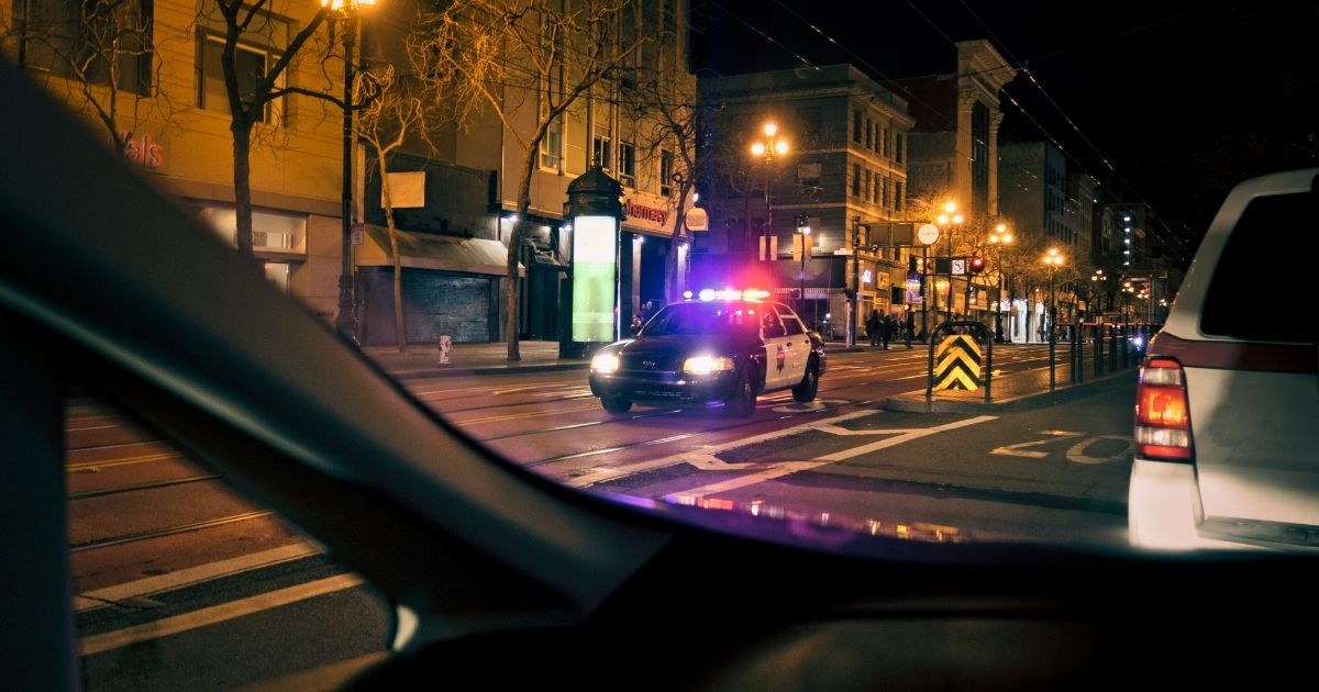 A police car drives with its lights on down a street at night