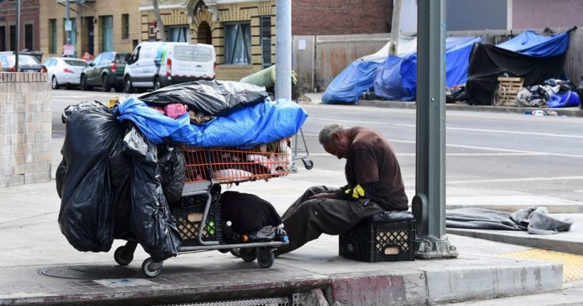 A homeless man sits beside his belongings on the streets in the Skid Row community of Los Angeles on April 26, 2021.
