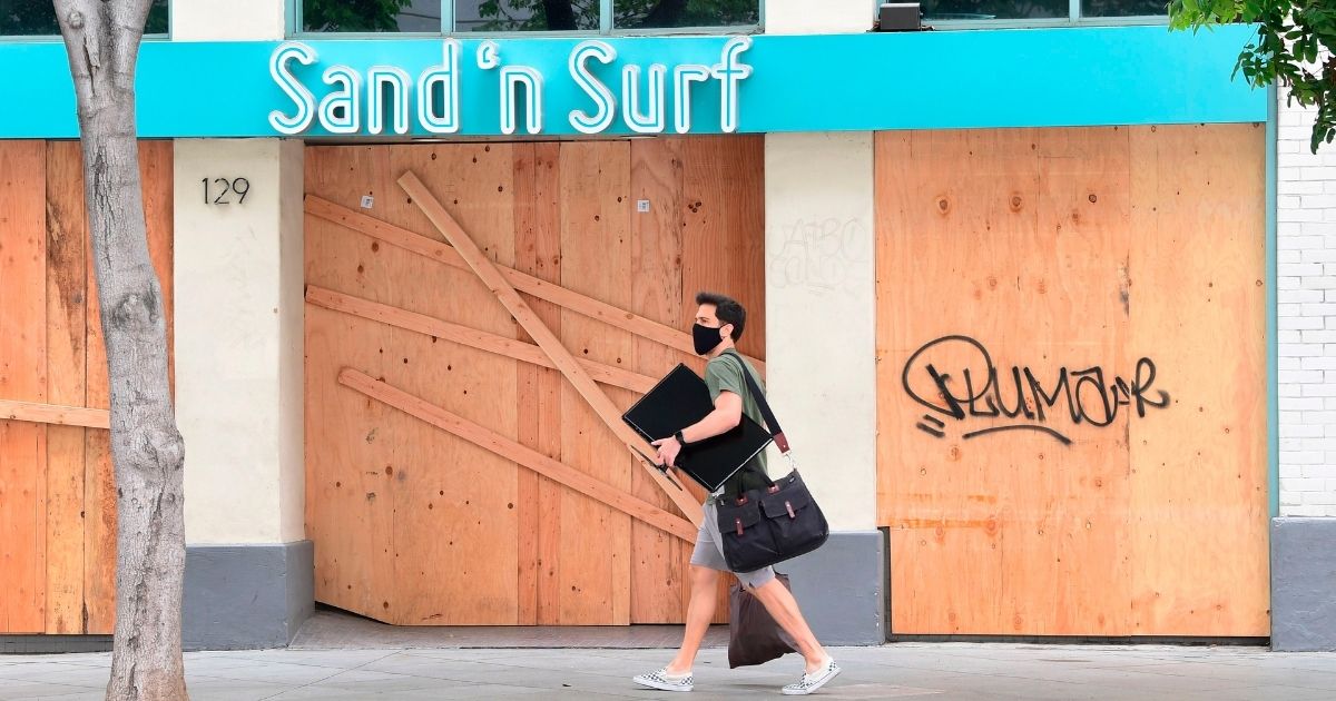 A man walks past a boarded-up Sand 'n Surf shop as many businesses were closed around the Third Street Promenade shopping district in Santa Monica, California, on June 26, 2020.