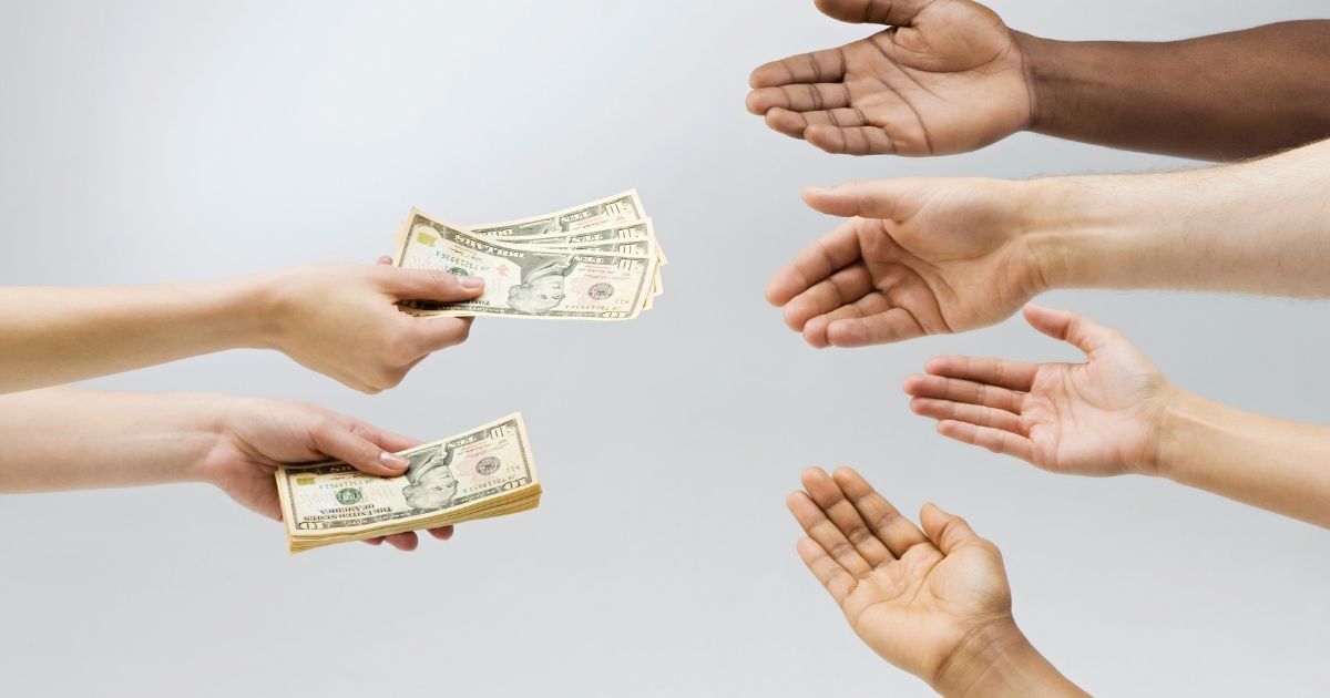 This stock photo portrays a person holding out money to outstretched hands. On Saturday, nine states will join Iowa, Mississippi and Missouri in ending their pandemic-related unemployment benefits early.