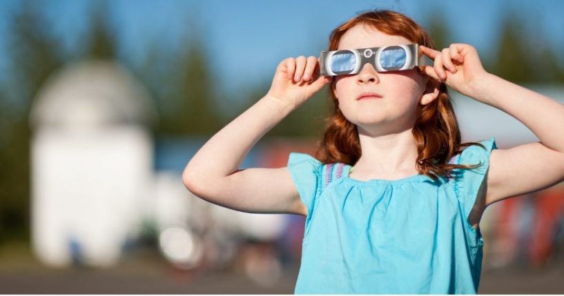 A young girl watches the annular solar eclipse with special viewing glasses.