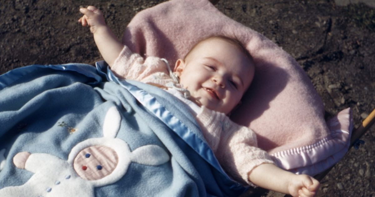 A 1994 film photo shows a baby girl of approximately one year wrapped in a blue bunny-themed blanket as she smiles.