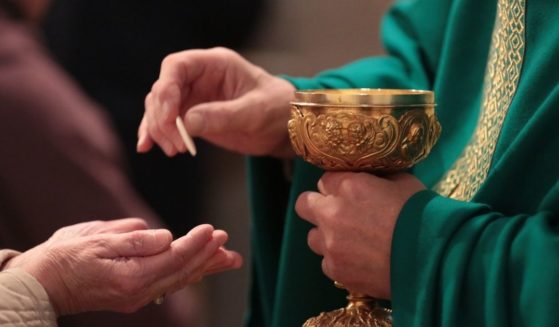 A priest administers communion in the above stock image.