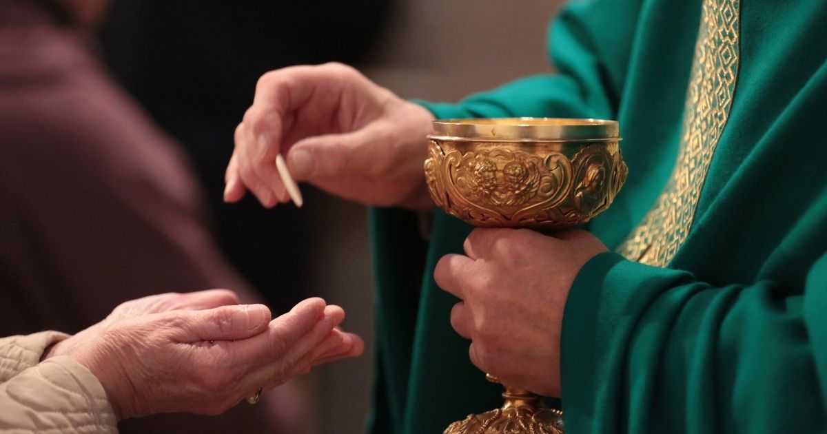 A priest administers communion in the above stock image.