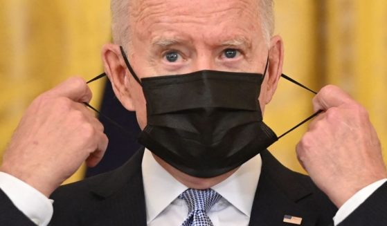 President Joe Biden takes off his face mask before speaking about COVID-19 vaccinations in the East Room of the White House in Washington on Thursday.