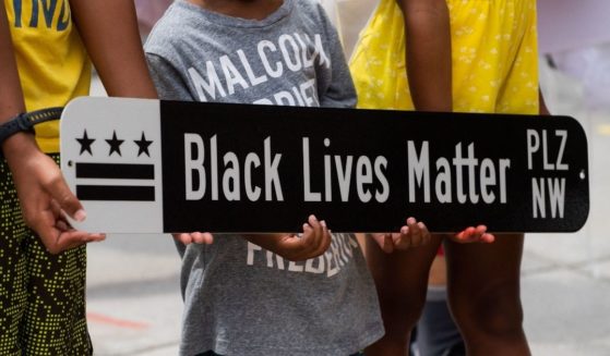 Children pose for a photograph with a Black Lives Matter Plaza street sign at Black Lives Matter Plaza in Washington, D.C., on June 19, 2021, during a Juneteenth celebration.