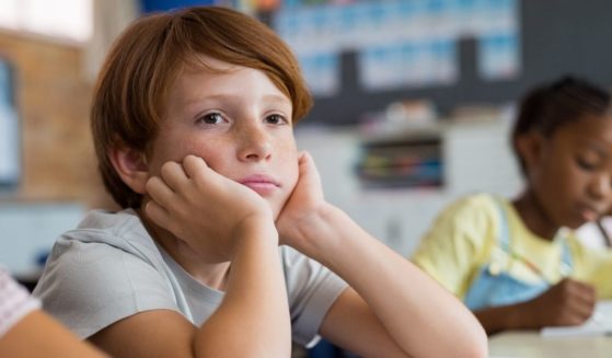 A boy looks tired and bored as he sits at his desk in a classroom.