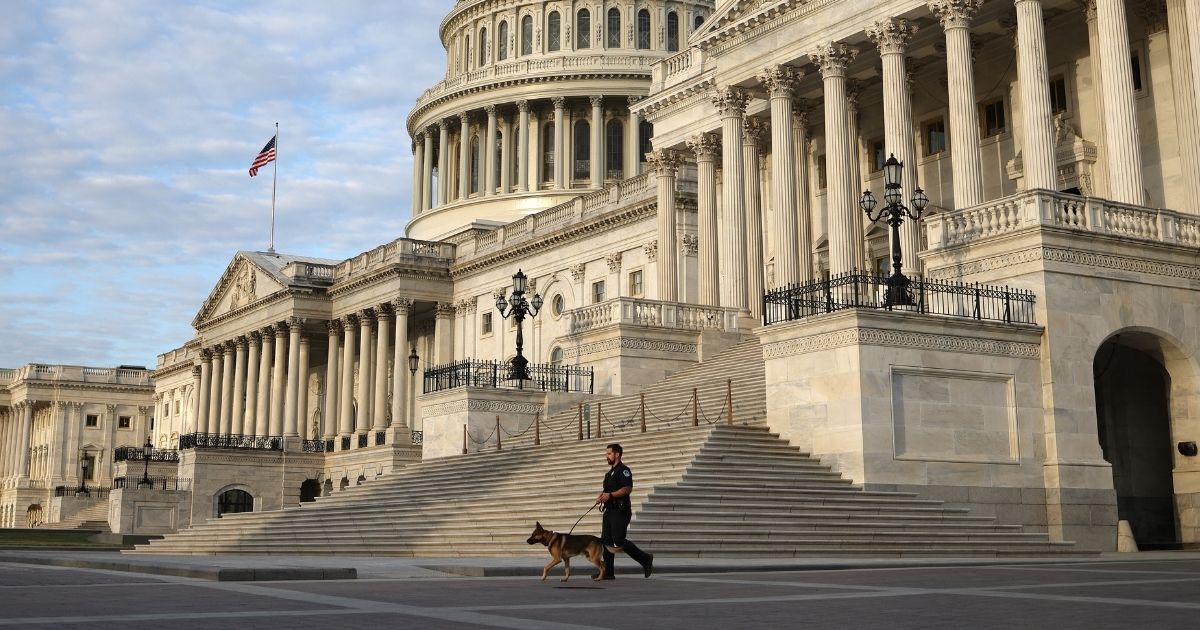 A Capitol Police Officer walks a police dog across the west front of the U.S. Capitol Building on May 14, 2021, in Washington, D.C.