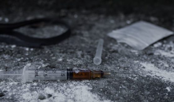 A syringe filled with dark liquid lays on top of white powder