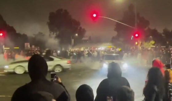 Hundreds of people crowd a traffic light as cars drive through