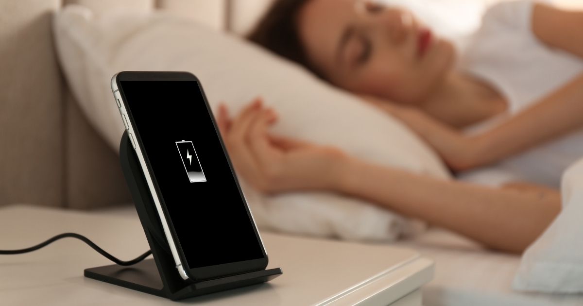 A person is pictured sleeping while her phone sits on a table next to her in the stock image above.
