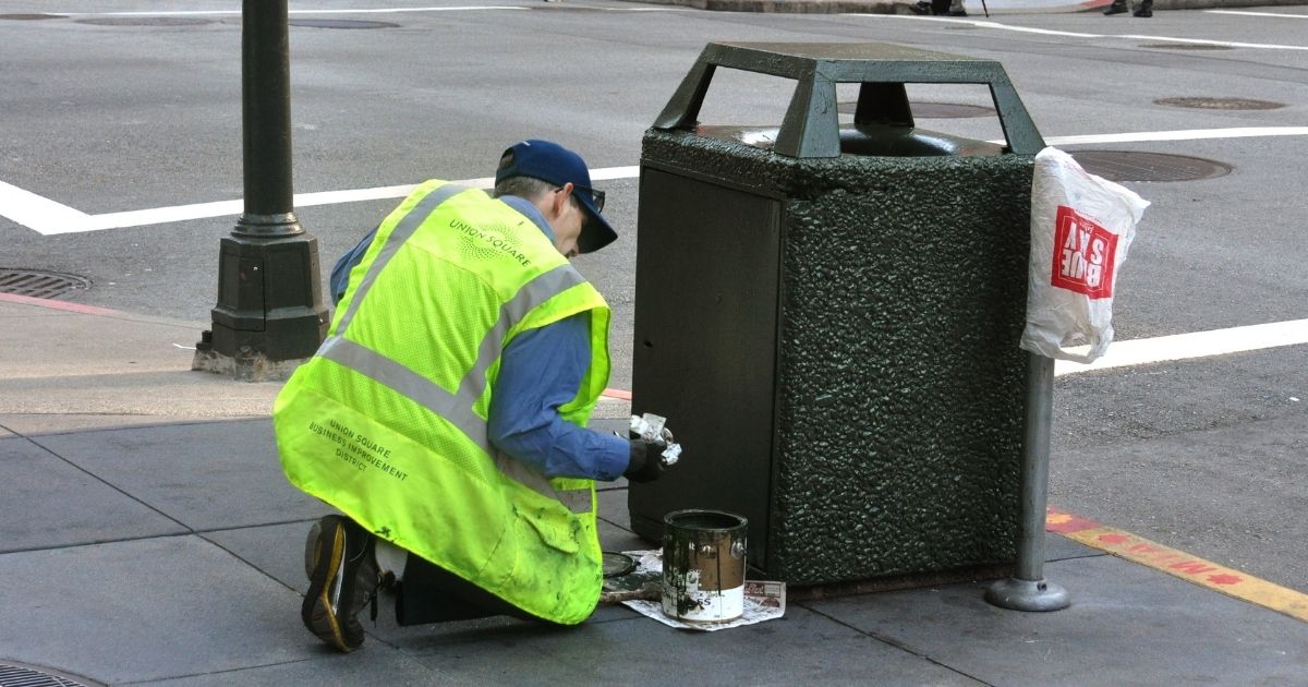 A city worker paints a trash receptacle