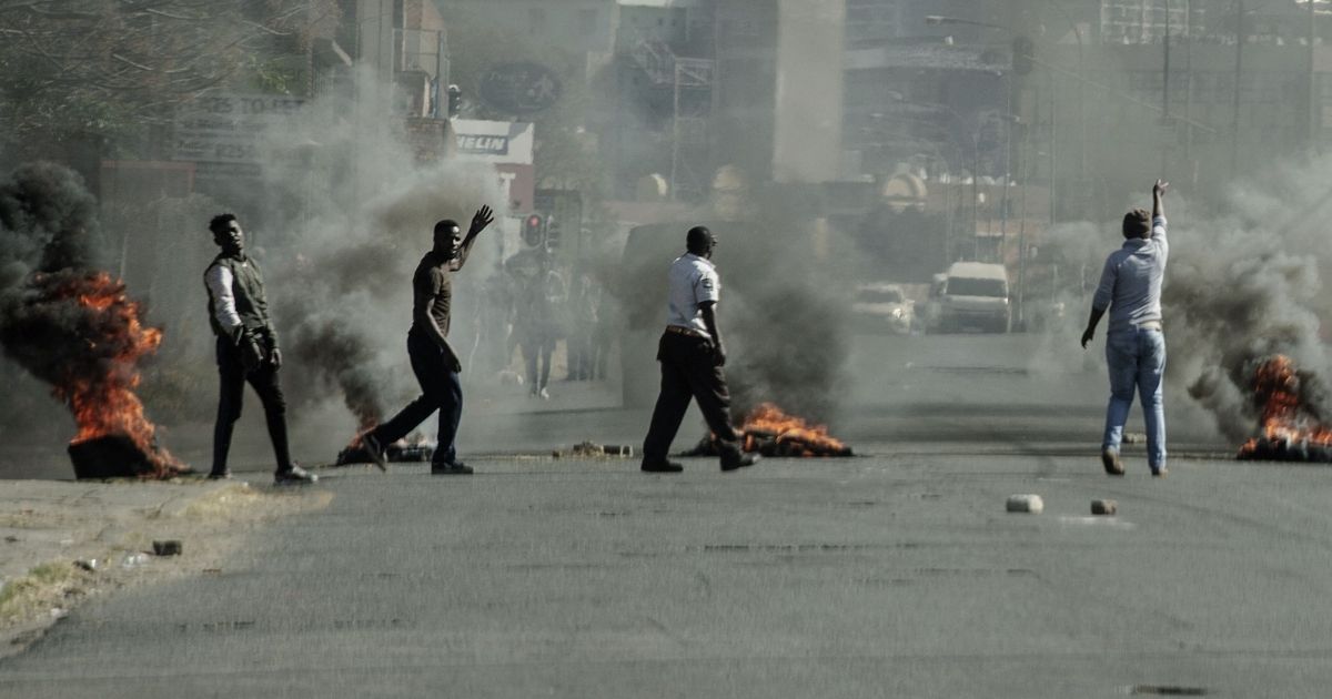 Protesters gesture toward police officers (not seen) as they burn tires in Jeppestown, Johannesburg, on Sunday.