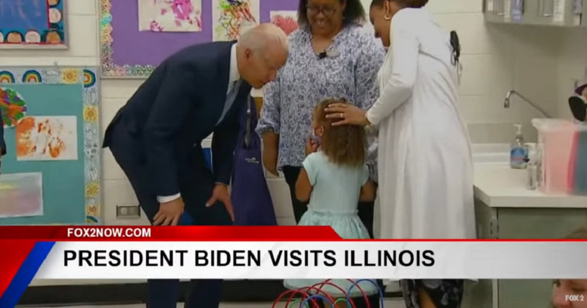 President Joe Biden bends down to speak to a little girl in a school setting.