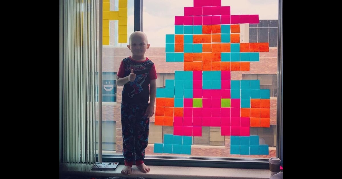 Meyer Mixdorf, 5, stands with one of the pieces he and his family made in a friendly battle of post-it note art that began during a stay at a hospital while he was treated for cancer.