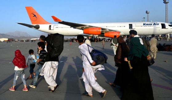 Afghan families walk by the aircrafts at the Kabul airport in Kabul