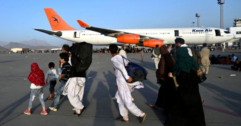 Afghan families walk by the aircrafts at the Kabul airport in Kabul
