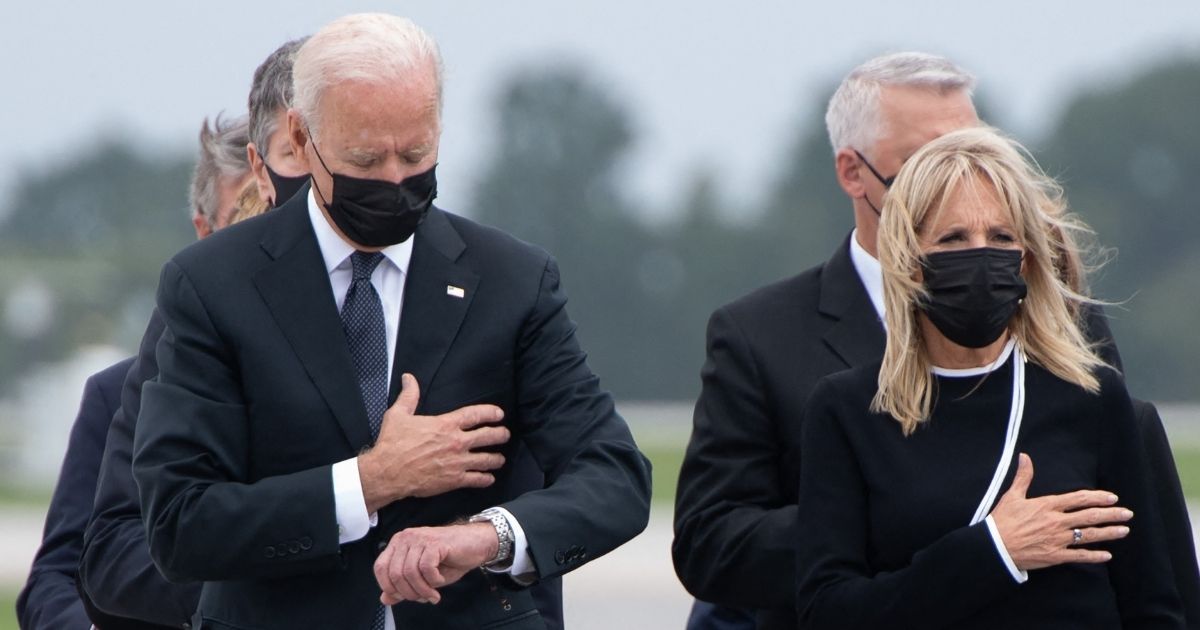 President Joe Biden appears to look down at his watch while standing alongside first lady Jill Biden during the dignified transfer of the remains of fallen service members at Dover Air Force Base in Delaware on Sunday.