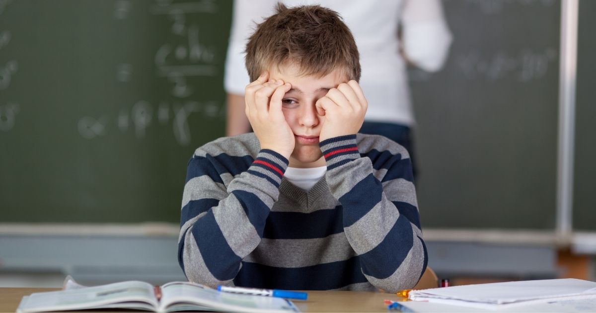 A boy sits in class with his hands on face.