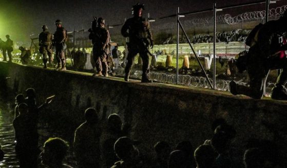 In this picture taken in the late hours on Sunday, British and Canadian soldiers stand guard near a canal as Afghans wait outside the foreign military-controlled part of the airport in Kabul hoping to flee the country following the Taliban's military takeover of Afghanistan.