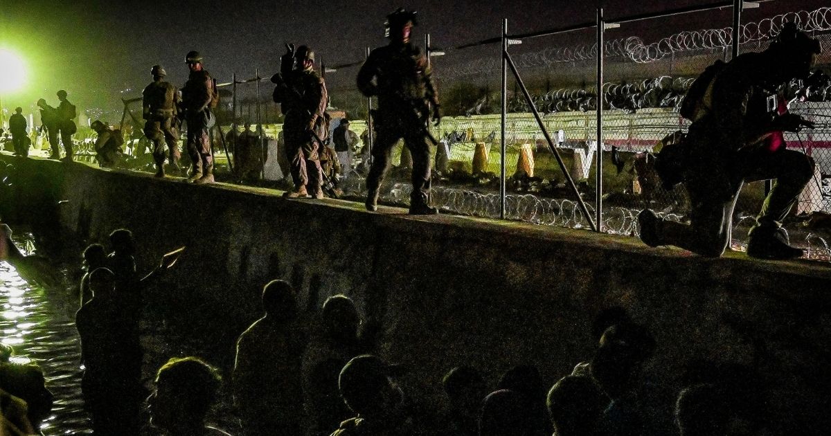 In this picture taken in the late hours on Sunday, British and Canadian soldiers stand guard near a canal as Afghans wait outside the foreign military-controlled part of the airport in Kabul hoping to flee the country following the Taliban's military takeover of Afghanistan.