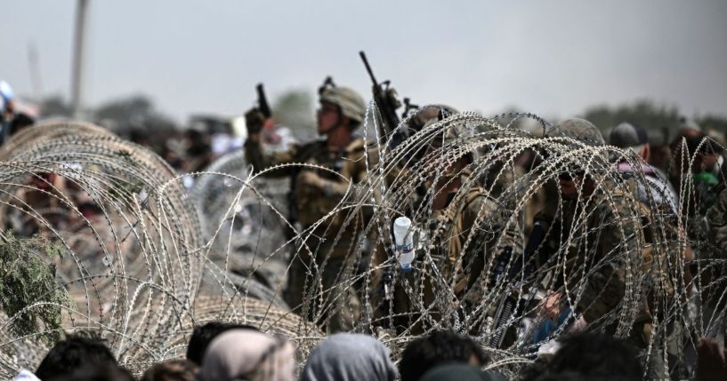 A U.S. soldier shoots in the air with his pistol while standing guard behind barbed wire as Afghans sit on a roadside near the military part of the airport in Kabul on August 20, 2021.