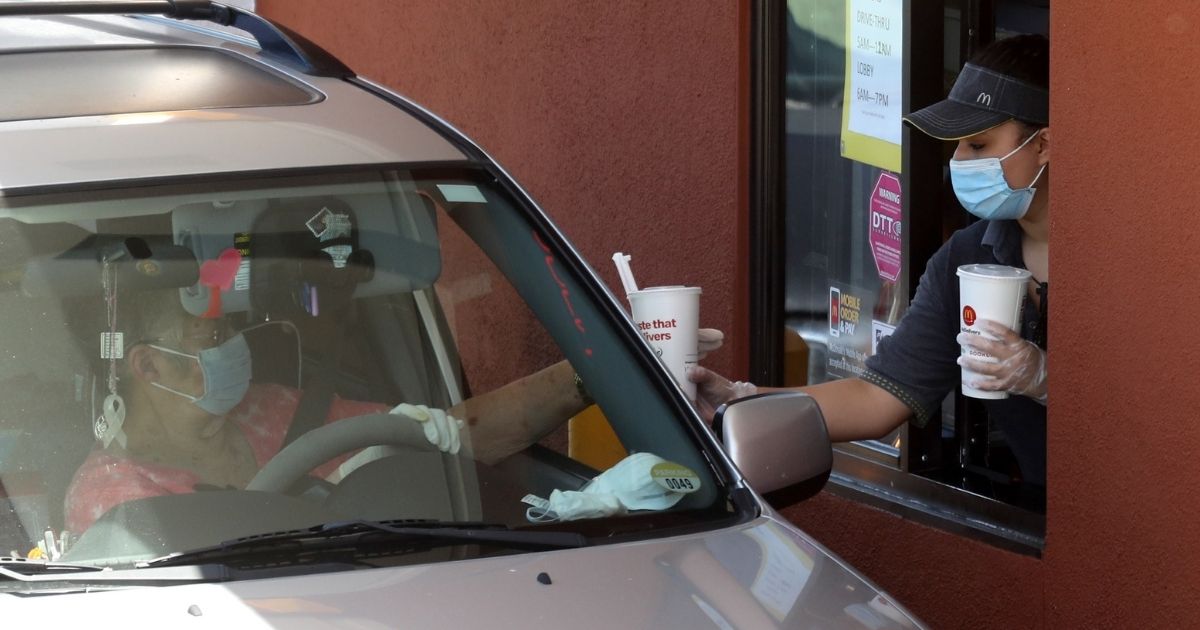 A McDonald's worker wears a mask and gloves as she hands soft drinks to a customer at a drive-thru in Novato, California, on April 22, 2020.